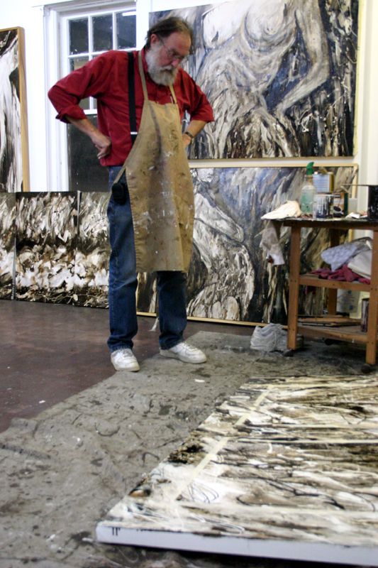 Artist in studio inspecting large abstract paintings