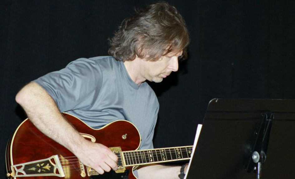 Person playing guitar beside sheet music stand