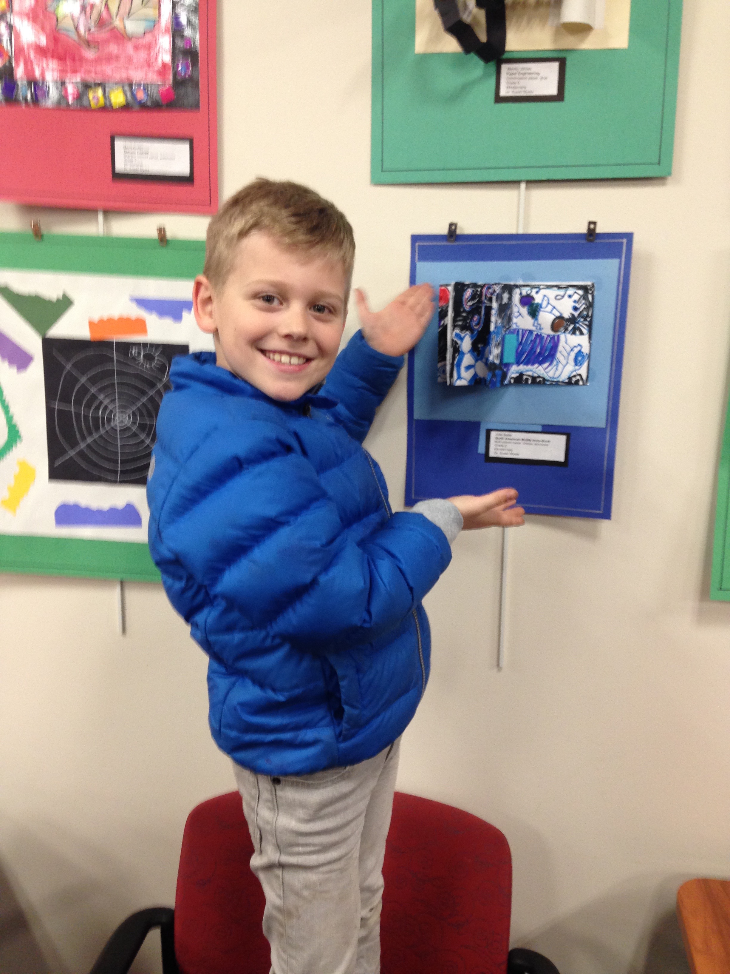Smiling boy in blue jacket pointing at artwork