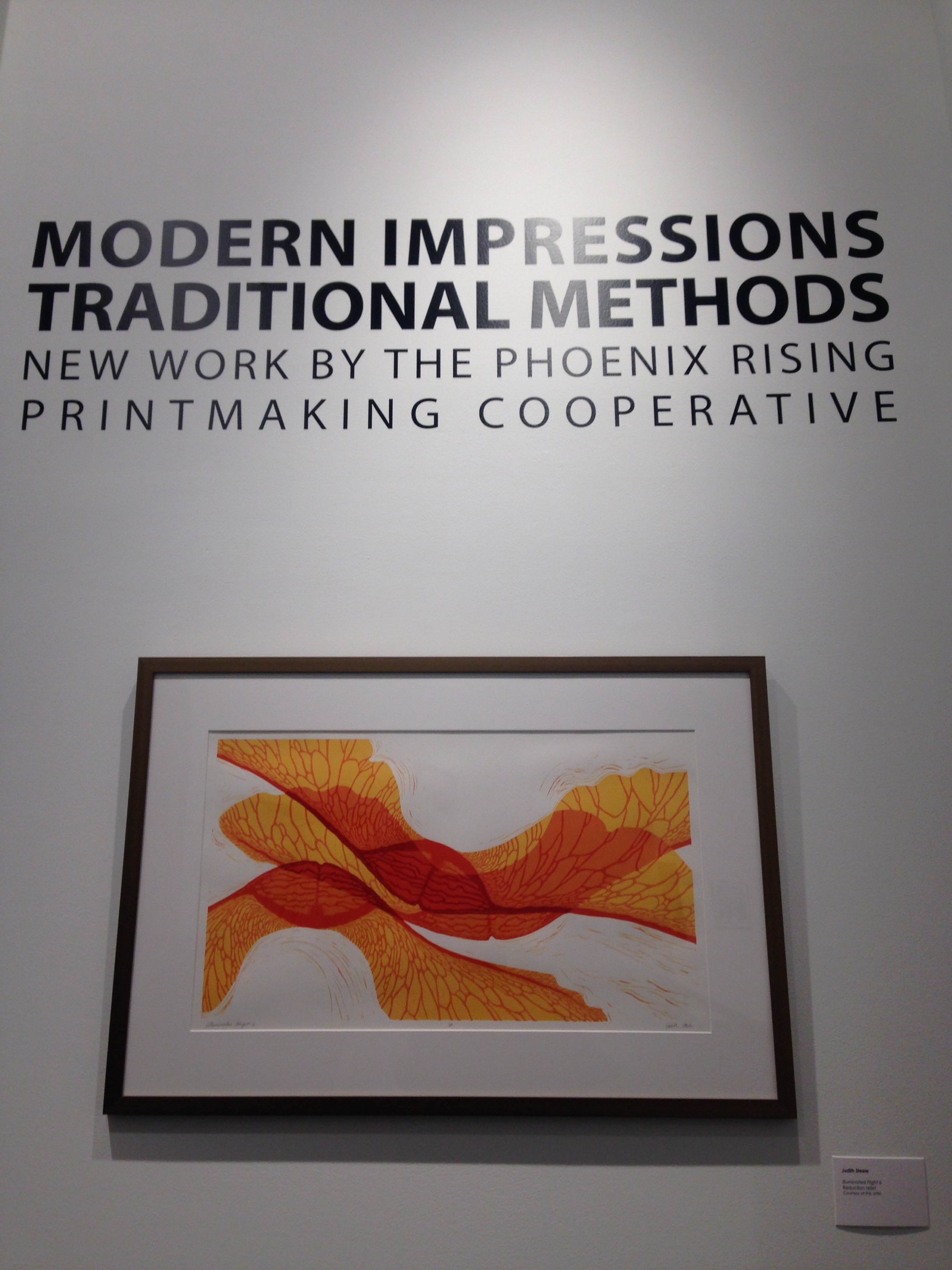 Framed abstract orange print beneath exhibition wall text