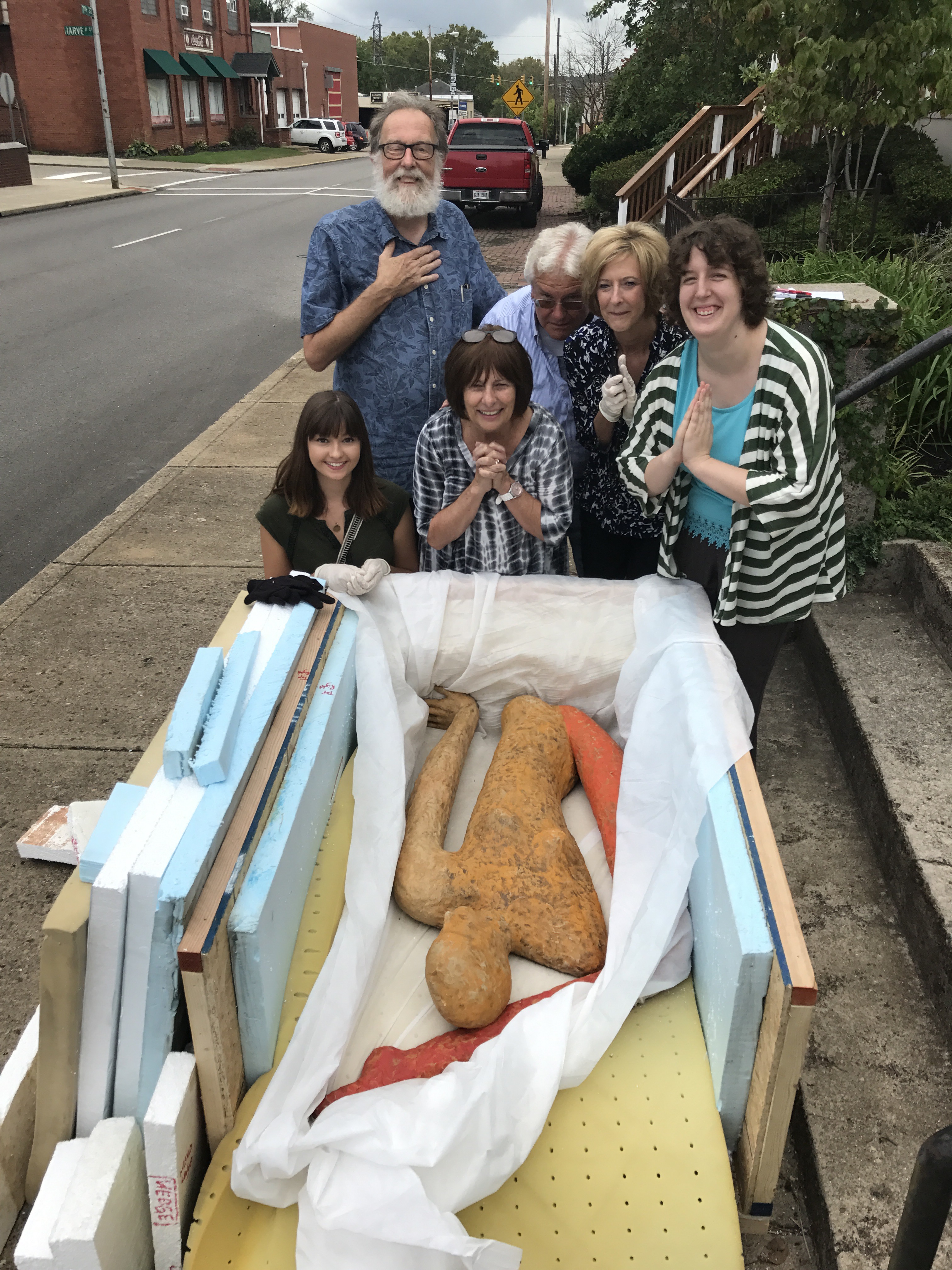 People gathered around wrapped humanoid sculpture on sidewalk