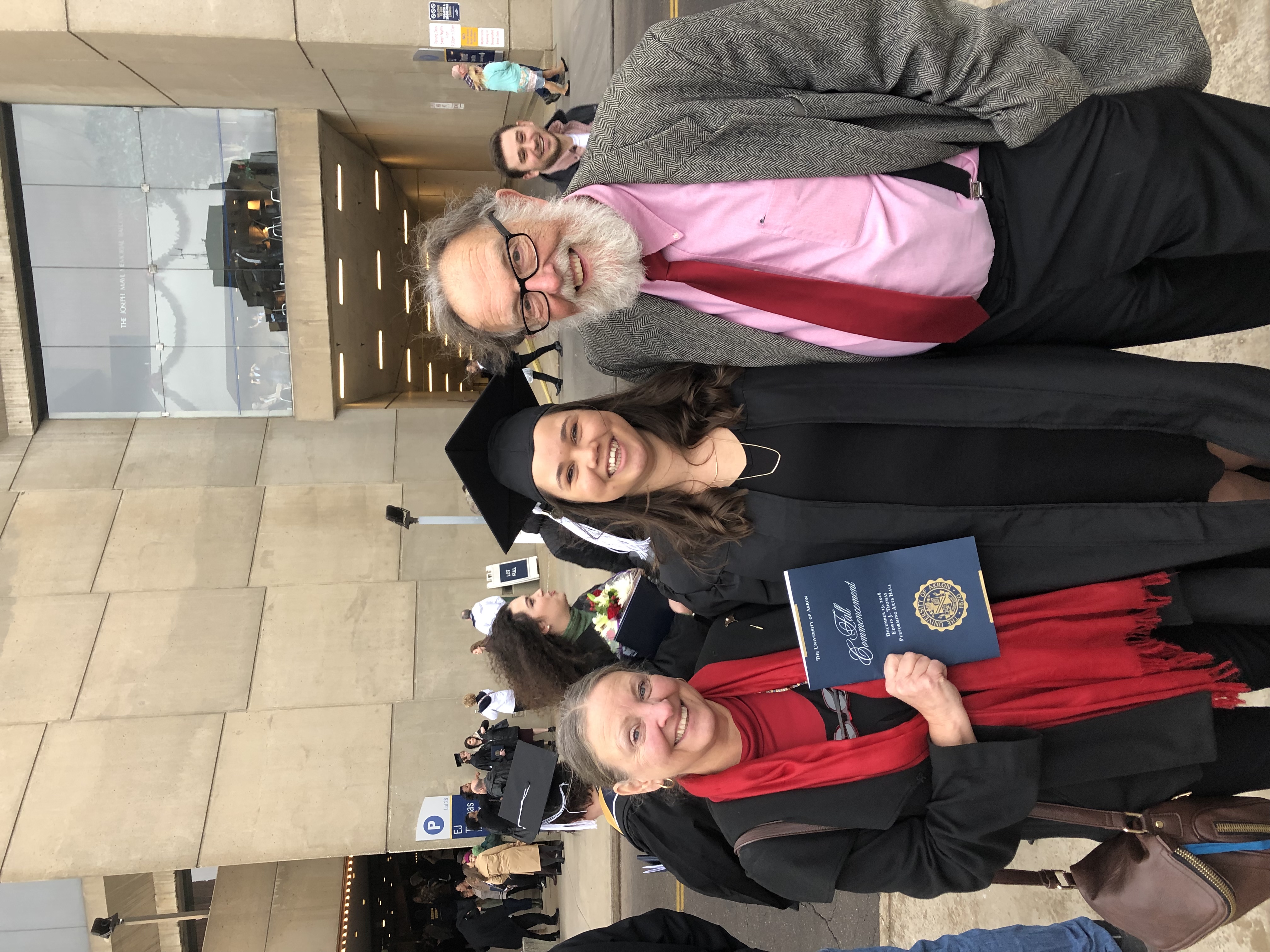 Graduate in cap and gown holding diploma, family